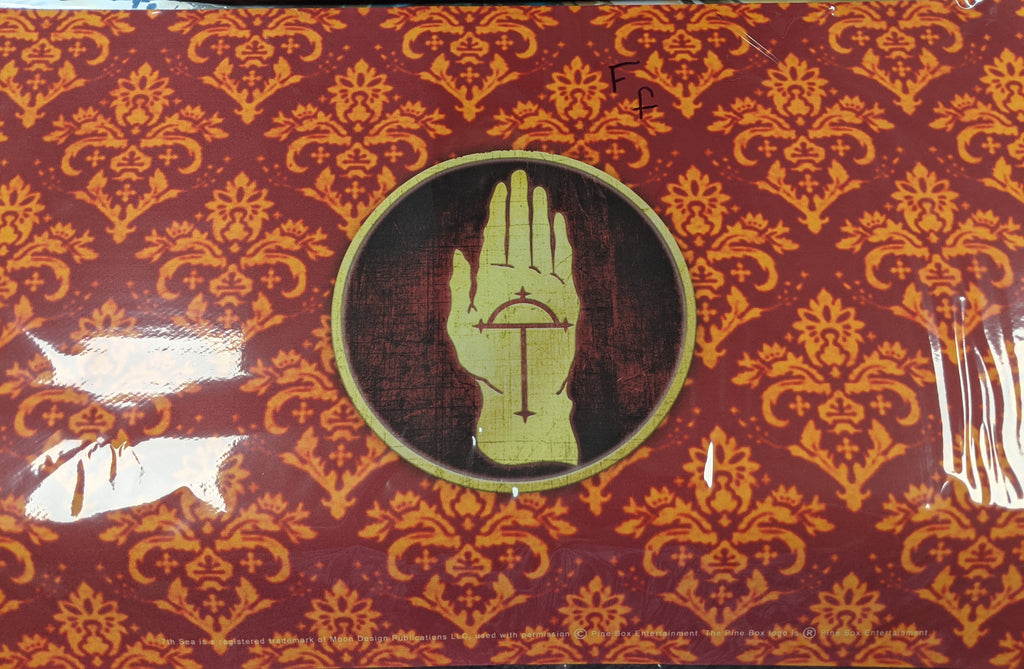 Red playmat with orange designs. The center is a logo of a yellow hand with a symbol on the palm.