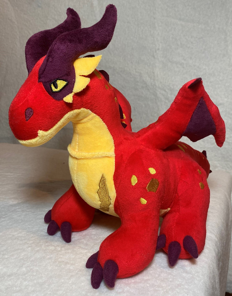 A red dragon plushie with a yellow belly, some yellow spots and maroon horns, claws, and inner wings..